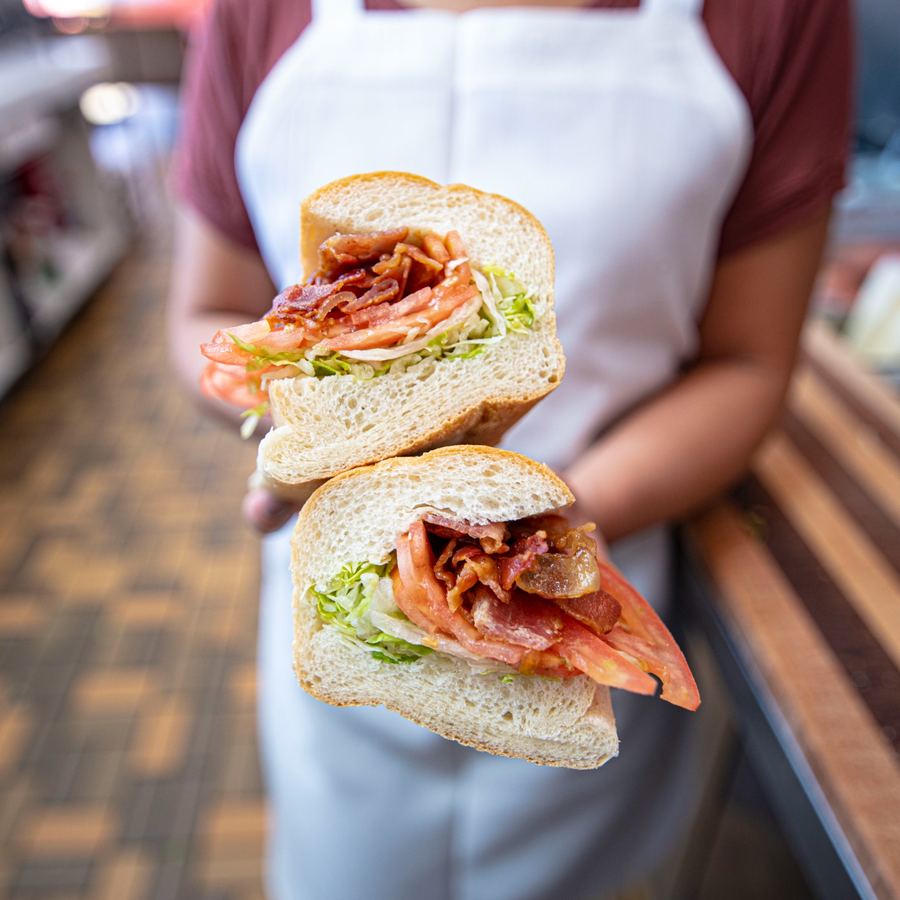 Crispy BLT sub on a cutting board showing thick-cut crispy bacon, fresh lettuce, and sliced tomato on a soft white roll