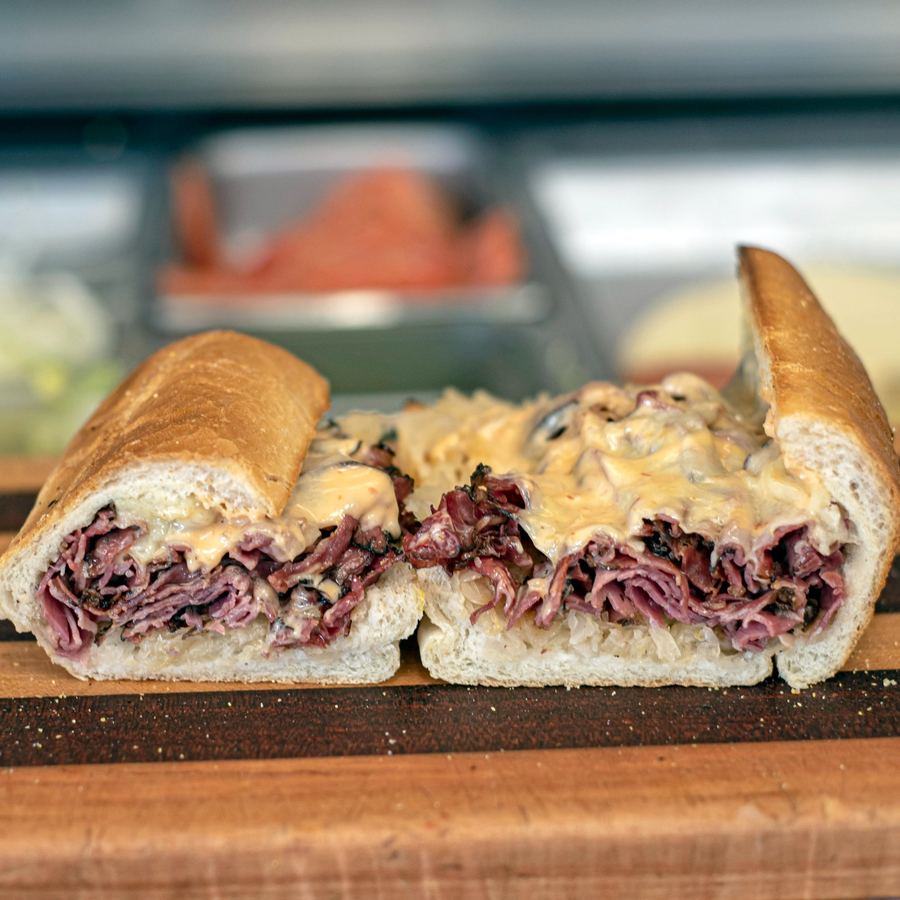Pastrami Reuben cut in half showing thick New York style black pastrami, melted swiss, sauerkraut, and Russian dressing