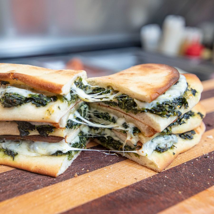 Riccotti's famous spinach pie pulled open showing gooey melted provolone, sauteed spinach, and pepperoni in a golden crust