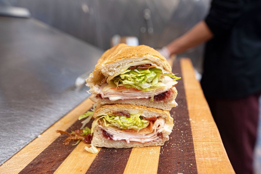 Turkey Special sub in cross-section showing layers of oven roasted turkey, bacon, melted provolone, cranberry sauce, lettuce, and tomato on fresh bread